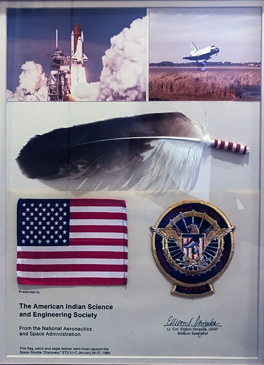Eagle feather with U.S. flag patch and photo of space shuttle.