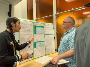 A young person shows an older person their science fair poster.